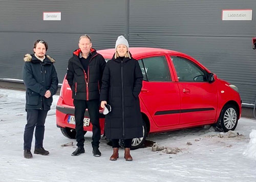 Tre vinterklädda personer framför en röd bil